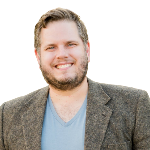 Smiling man wearing a brown blazer over a light blue V-neck shirt, portrait on a white background.